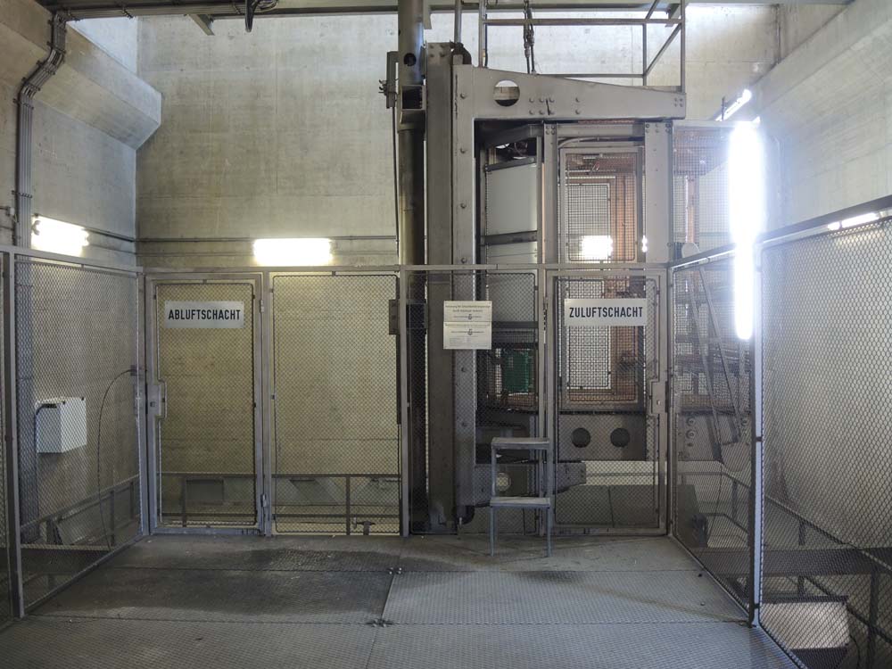 Industrieanlage mit Metallgittern und Beschilderung für Abluft- und Zuluftschächte in einem technischen Gebäude mit Betonwänden